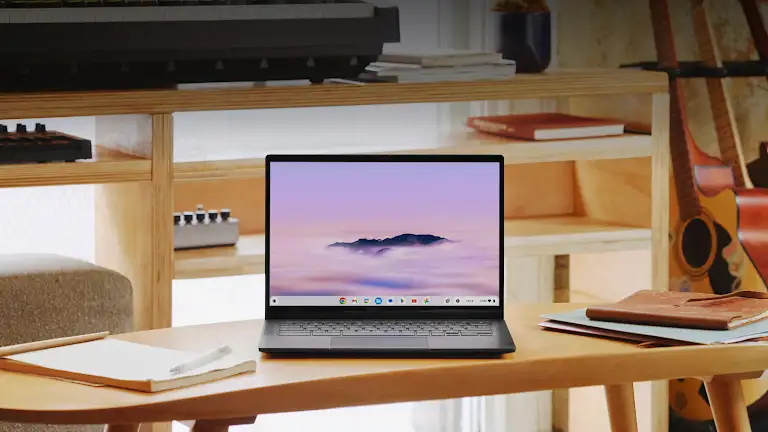 A Google Chromebook sits on a counter next to notebooks and a pen and paper.